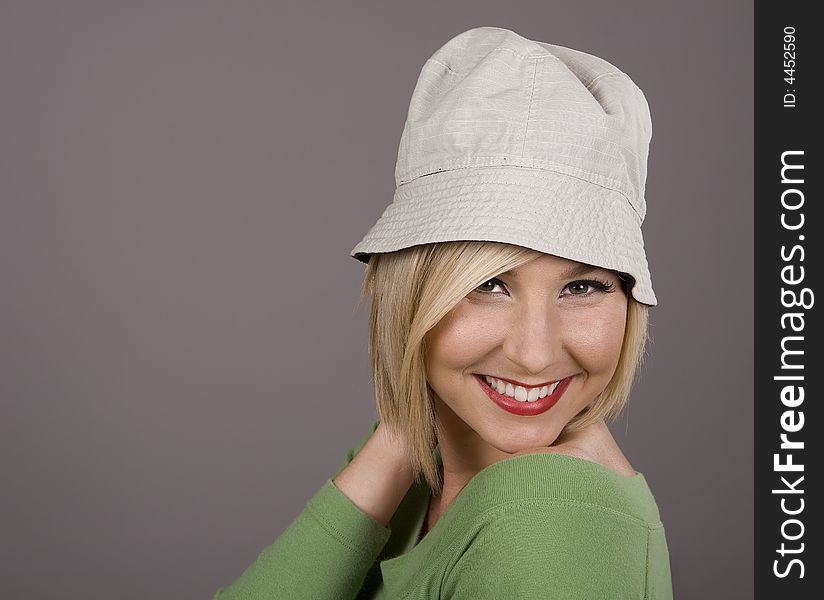 A blonde in a green blouse and silly white hat smiling with her hand behind her head. A blonde in a green blouse and silly white hat smiling with her hand behind her head