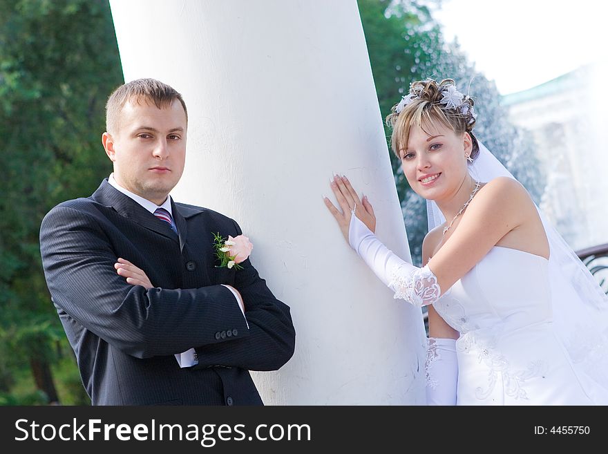 A bride and a groom stand by a white column. A bride and a groom stand by a white column