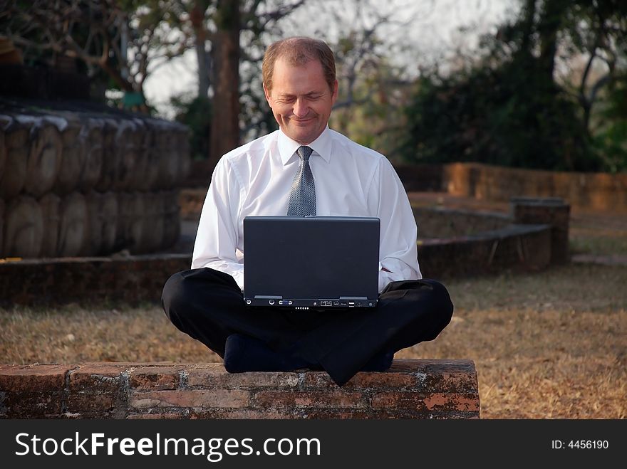 A middle aged man working on a computer in a park. A middle aged man working on a computer in a park