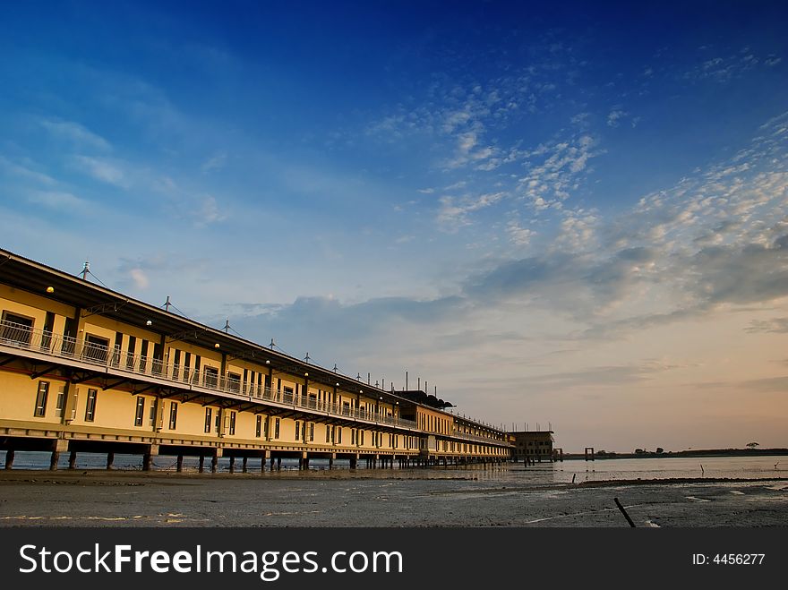 Long linear building on stilts built over muddy flats as a beach resort as seen at low tide and at sunset. Long linear building on stilts built over muddy flats as a beach resort as seen at low tide and at sunset