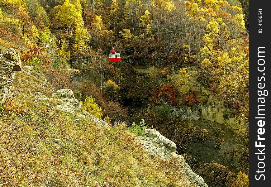 The red car of ropeway on a background of an autumn woods