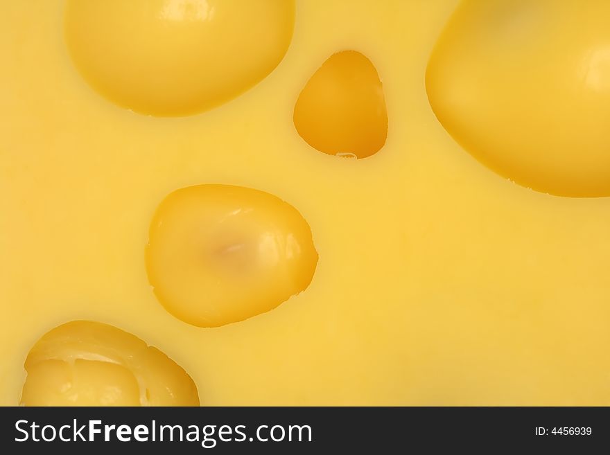 An extreme close-up of yellow cheese with big wholes.