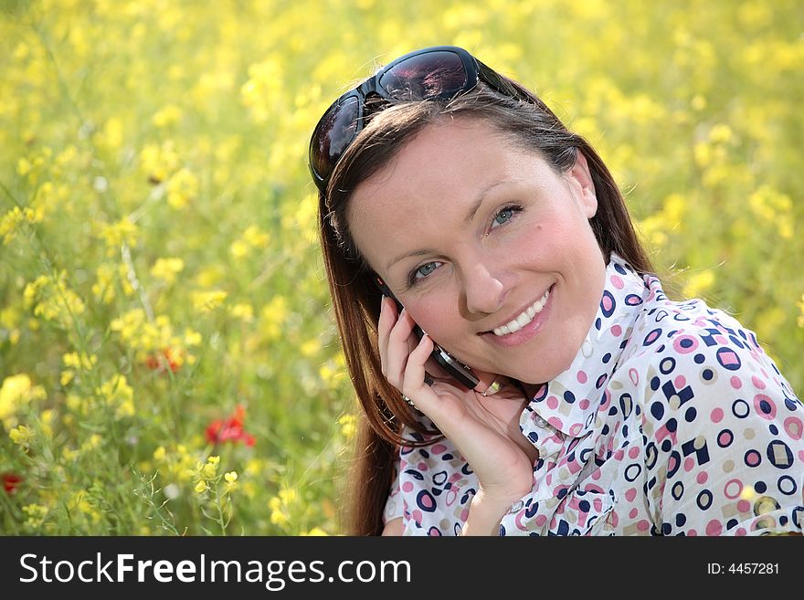 Pretty young woman talking on mobile phone on a meadow smiling