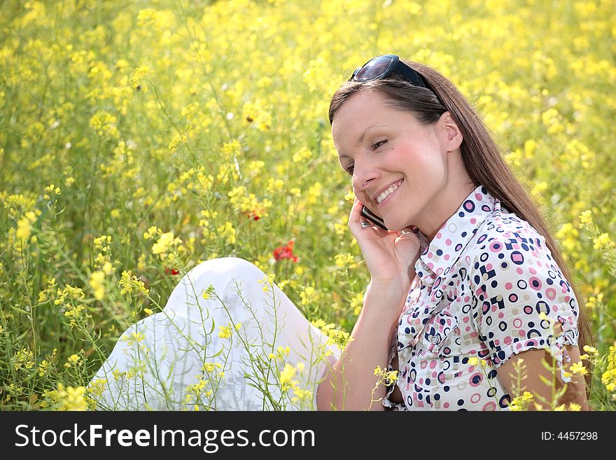 Pretty young woman talking on mobile phone on a meadow smiling