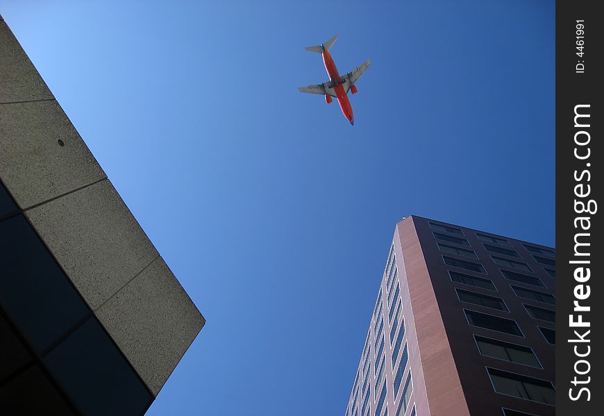 Looking up between buildings at airplane flying over city