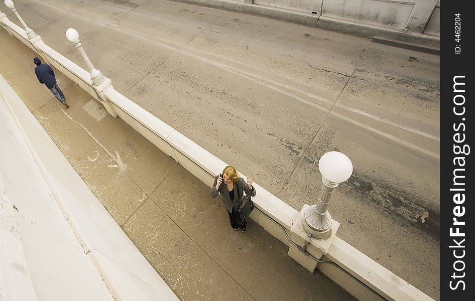 Wide shot from above of  woman on her cell phone next to an empty road. Wide shot from above of  woman on her cell phone next to an empty road.