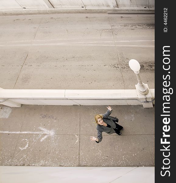 Wide shot from above of woman on a sidewalk with her hands in the air