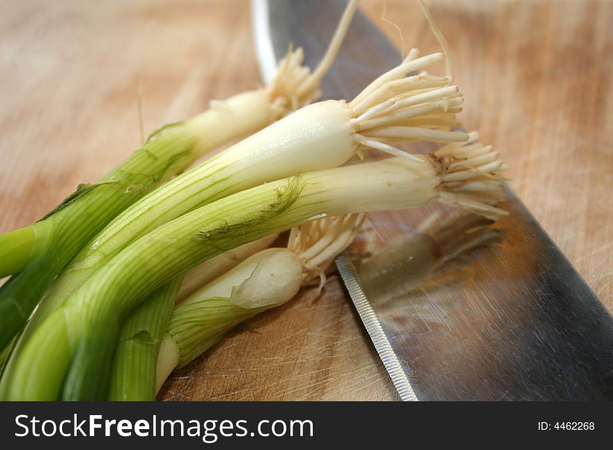 A group of fresh green onions sit close to a knife on a cutting board. A group of fresh green onions sit close to a knife on a cutting board.