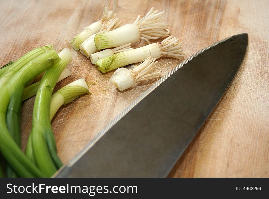 A group of fresh green onions have been cut and are sitting next to a knife on a cutting board. A group of fresh green onions have been cut and are sitting next to a knife on a cutting board.