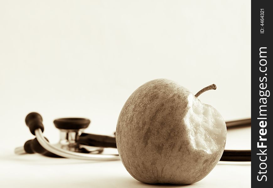 Still life of a single apple with a bite missing and an out of focus stethoscope suggesting the apple keeping away the doctor. Still life of a single apple with a bite missing and an out of focus stethoscope suggesting the apple keeping away the doctor.