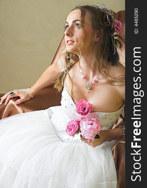 Beautiful happy young bride with long brown hair in white tule petticoat and vinateg and antique accessories sitting on a chair holding pink spring peony. Beautiful happy young bride with long brown hair in white tule petticoat and vinateg and antique accessories sitting on a chair holding pink spring peony