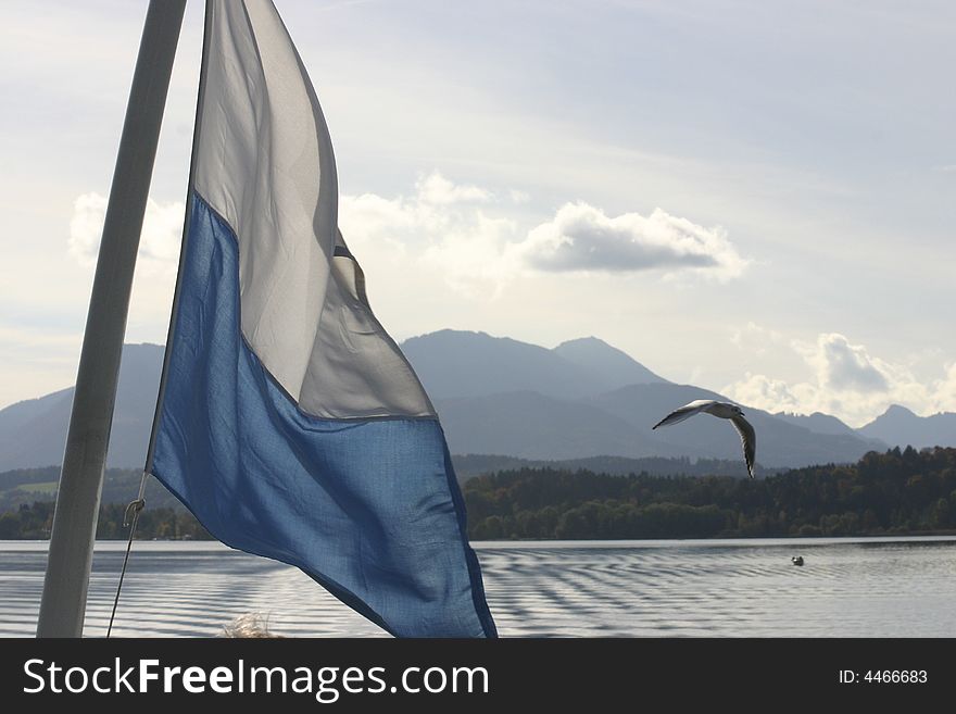 Bavarian flag on aft of boat, with mountains in background and seagull flying past. Bavarian flag on aft of boat, with mountains in background and seagull flying past