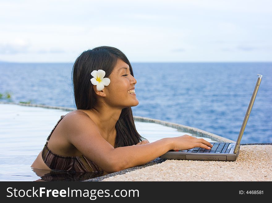Attractive young asian business woman working remotely on a laptop computer beside an infinity pool at a private tropical resort paradise vacation. Room for text. Attractive young asian business woman working remotely on a laptop computer beside an infinity pool at a private tropical resort paradise vacation. Room for text.