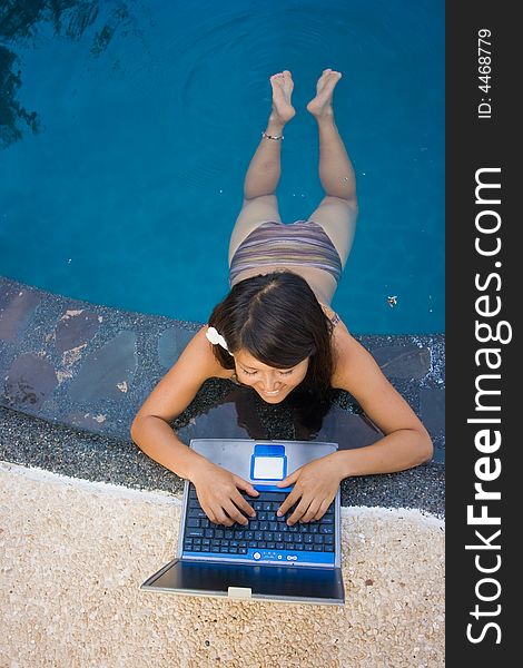 Attractive young Asian business woman working remotely on a laptop computer beside an infinity pool at a private tropical resort paradise vacation. Room for text. Attractive young Asian business woman working remotely on a laptop computer beside an infinity pool at a private tropical resort paradise vacation. Room for text.