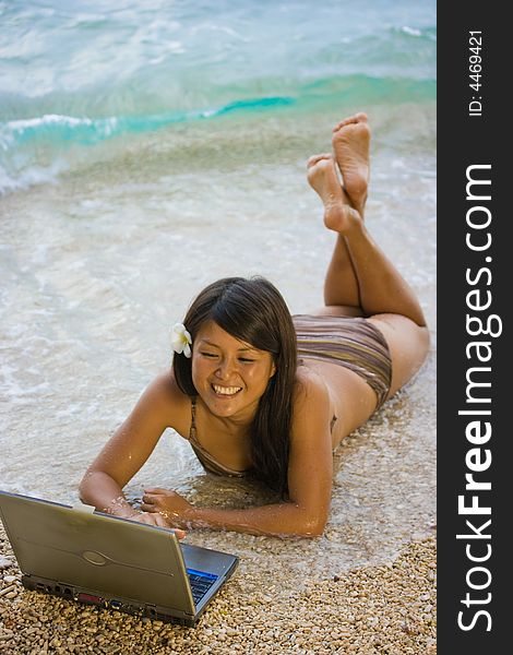Attractive young Asian business woman working remotely on a laptop computer at a private white sand beach beside the sea in the surf at a tropical resort paradise vacation. Room for text. Attractive young Asian business woman working remotely on a laptop computer at a private white sand beach beside the sea in the surf at a tropical resort paradise vacation. Room for text.