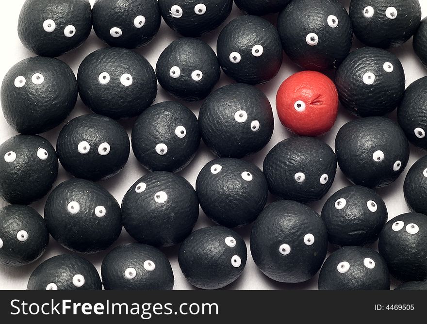 The idea of being different, distinguished among the others. Little plasticine balls with eyes. The red one is winking. White background. The idea of being different, distinguished among the others. Little plasticine balls with eyes. The red one is winking. White background.