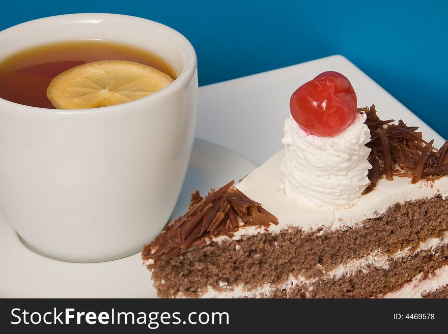 Cup of tea with lemon and cake on blue background