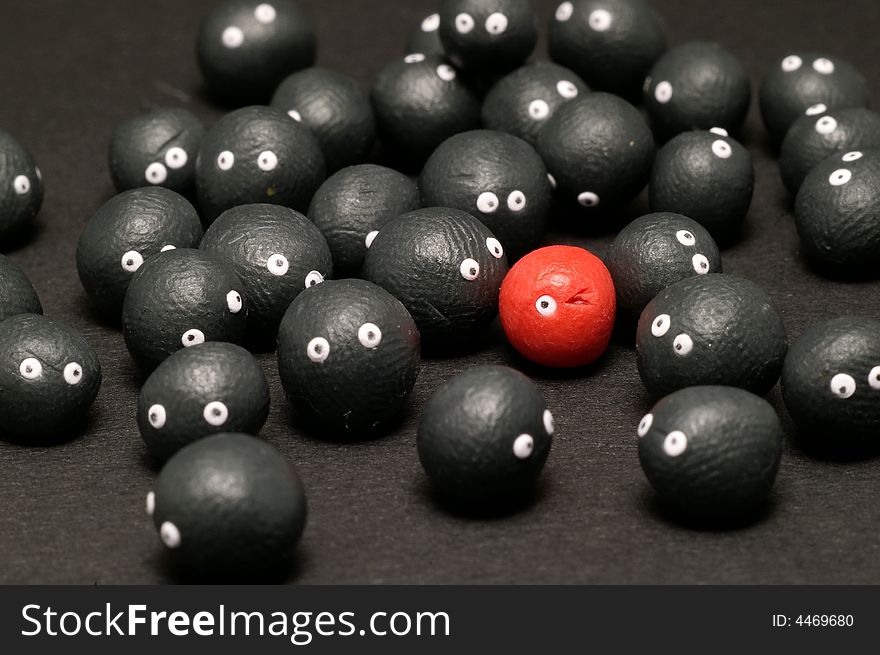 The idea of being different, distinguished among the others. Little plasticine balls with eyes. The red one is winking. Black background. The idea of being different, distinguished among the others. Little plasticine balls with eyes. The red one is winking. Black background.