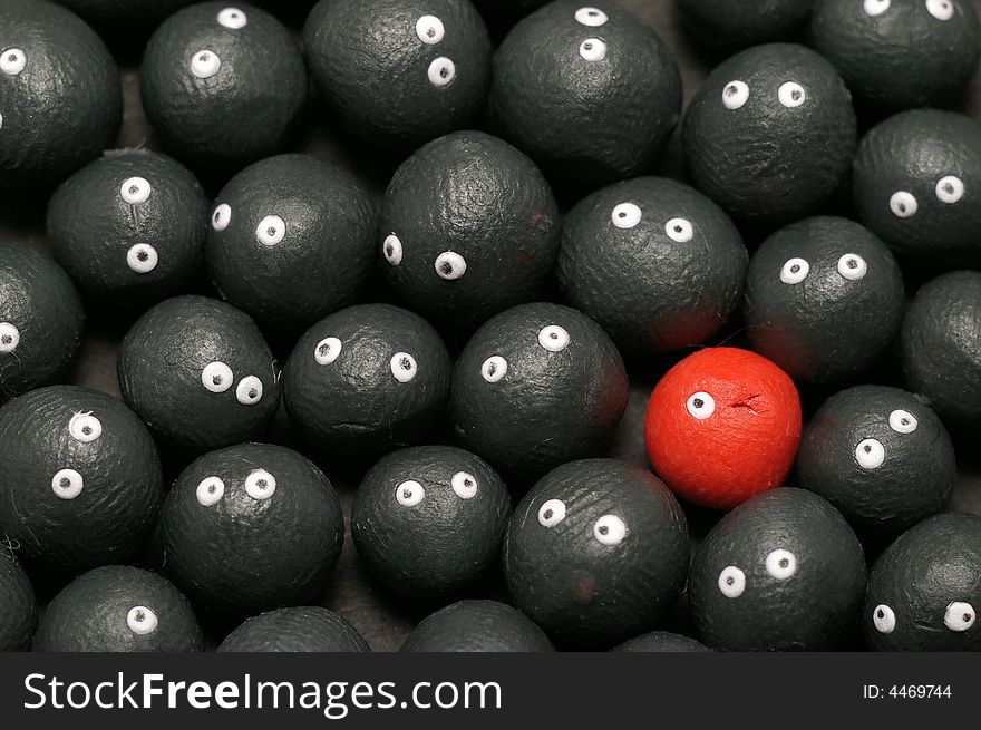 The idea of being different, distinguished among the others. Little plasticine balls with eyes. The red one is winking. Black background. The idea of being different, distinguished among the others. Little plasticine balls with eyes. The red one is winking. Black background.