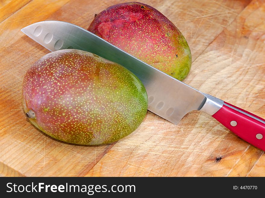 Two mangos on cutting board with knife in the middle. Two mangos on cutting board with knife in the middle