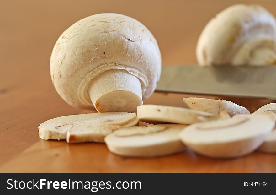 Mushrooms being sliced on a wood cutting board with stainless steel knife edge in frame. Mushrooms being sliced on a wood cutting board with stainless steel knife edge in frame.
