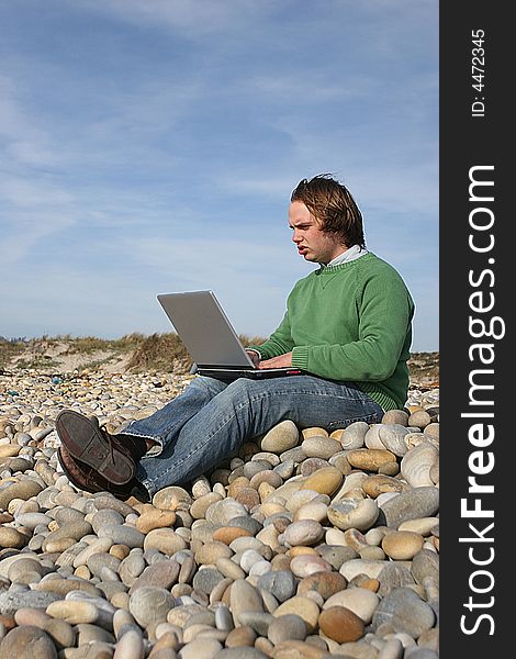 Young casual man with laptop at the beach