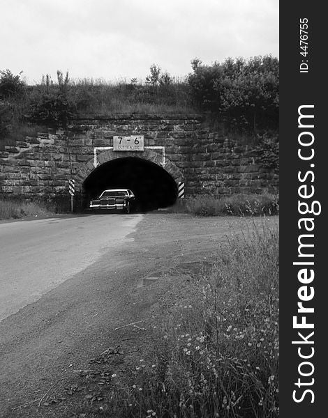 A car emerges out of the blackness of a tunnel that looks to go on forever. A car emerges out of the blackness of a tunnel that looks to go on forever