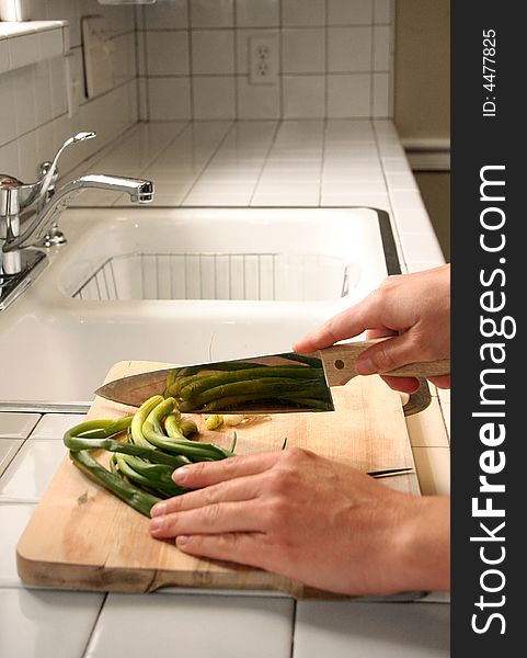 A person cuts fresh green onions on a wooden cutting board in the kitchen. A person cuts fresh green onions on a wooden cutting board in the kitchen.