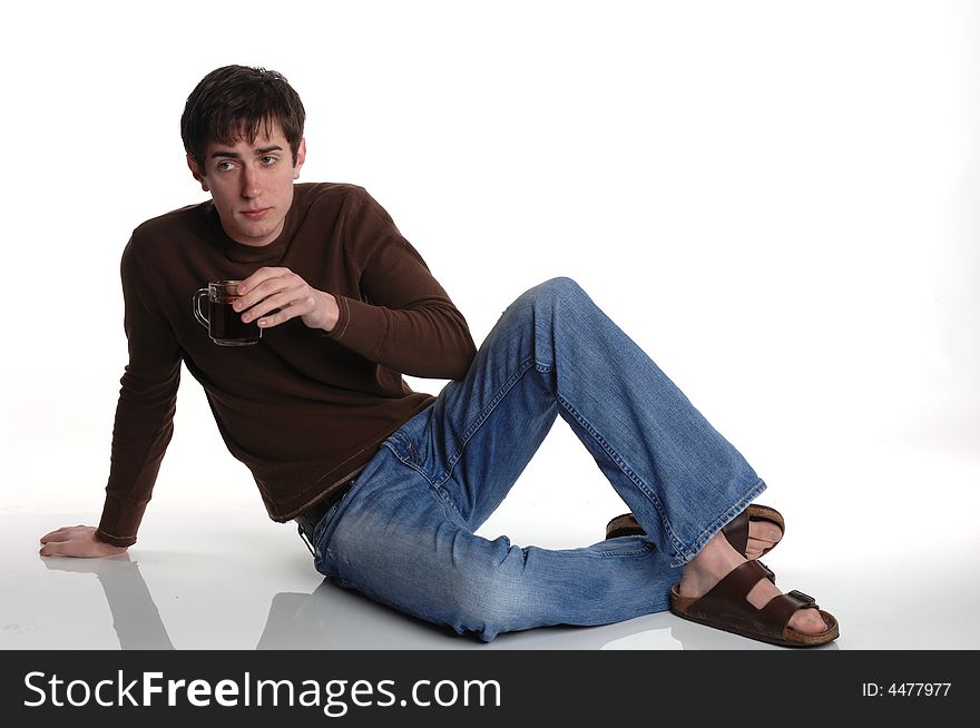 Young dark haired man sitting in jeans sandals and dark shirt holding coffee looking to viewers right. Young dark haired man sitting in jeans sandals and dark shirt holding coffee looking to viewers right