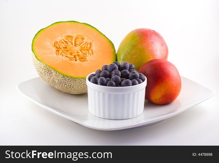 Cantaloupe,blueberries,mango and a nectarine share space on a white plate. Cantaloupe,blueberries,mango and a nectarine share space on a white plate.