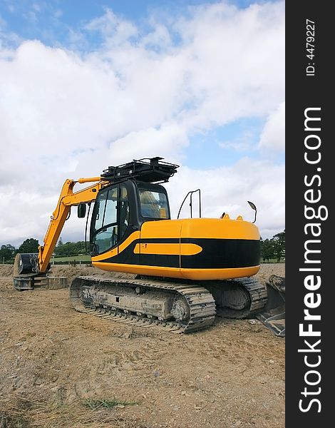 Rear view of a yellow industrial digger standing idle on rough ground. Rear view of a yellow industrial digger standing idle on rough ground.