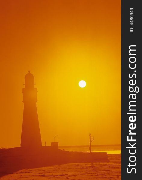 A lighthouse is engulfed by the orange glow of the sun through the fog. A lighthouse is engulfed by the orange glow of the sun through the fog