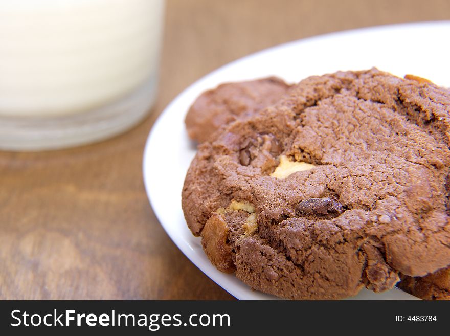 A plate of chocolate cookies with a glass of milk in the background. A plate of chocolate cookies with a glass of milk in the background.