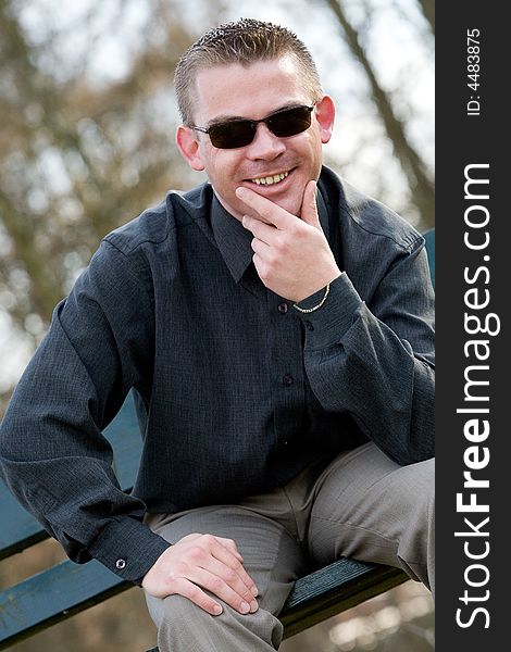 Young man is sitting on a bench in a park. Young man is sitting on a bench in a park