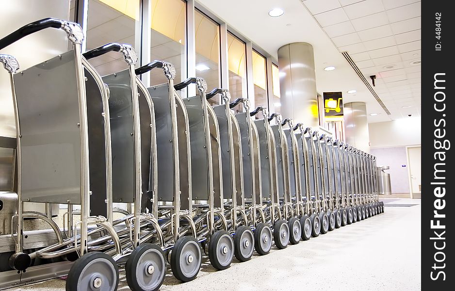 Row of luggage carts at busy airport, with selective focus on the closer carts.