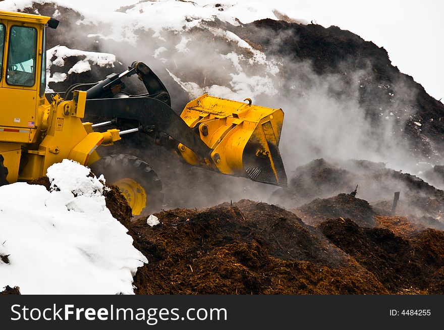 Action shot of front-end loader working in massive piles of steaming mulch and snow. Action shot of front-end loader working in massive piles of steaming mulch and snow