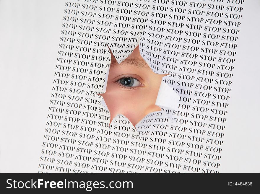 Eye looks into the hole in the sheet of paper with the printed word stop