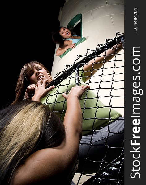 A female is hanging on to a fence as another female is prying her fingers off to fall. A female is hanging on to a fence as another female is prying her fingers off to fall.