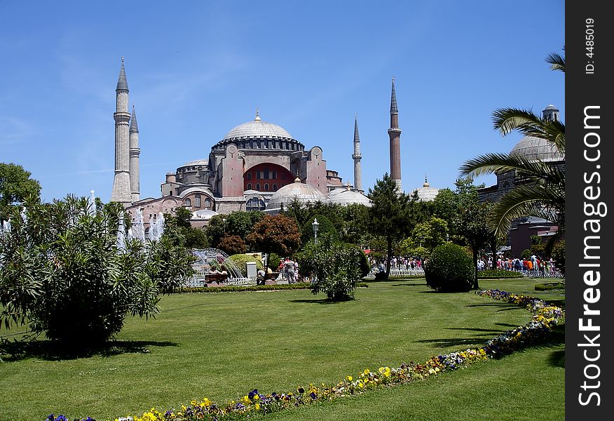 Byzantine landmark church Hagia Sophia converted to a mosque by the Ottomans behind trees, green grass, and colorful pansies, in Istanbul under blue sky. Byzantine landmark church Hagia Sophia converted to a mosque by the Ottomans behind trees, green grass, and colorful pansies, in Istanbul under blue sky