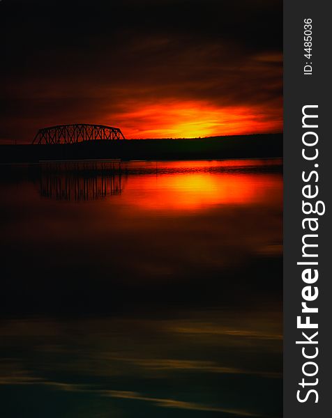 The last light of the sun glows on the horizon and is reflected in a calm lake along with a trestle bridge. The last light of the sun glows on the horizon and is reflected in a calm lake along with a trestle bridge