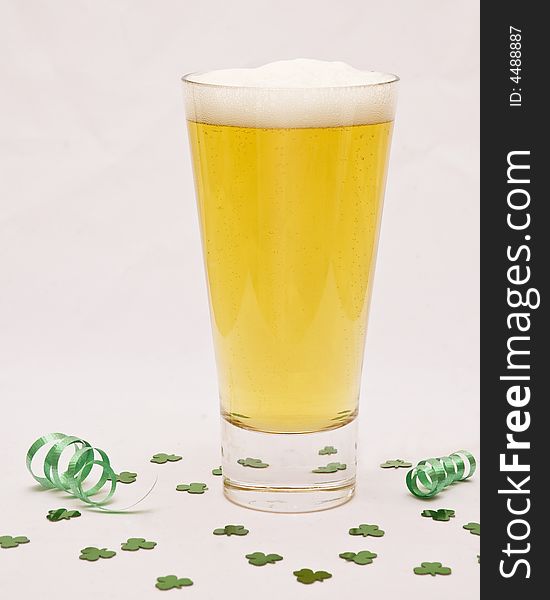 A tall glass of beer against a white background with shamrock confetti around it. A tall glass of beer against a white background with shamrock confetti around it