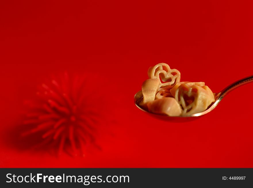 Heart-shaped pasta on a metal spoon against a red background. Heart-shaped pasta on a metal spoon against a red background.