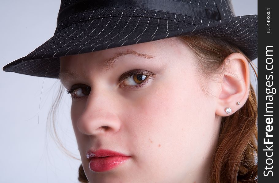 Serious teen peering out from under the brim of her pin-striped fedora hat. Serious teen peering out from under the brim of her pin-striped fedora hat.