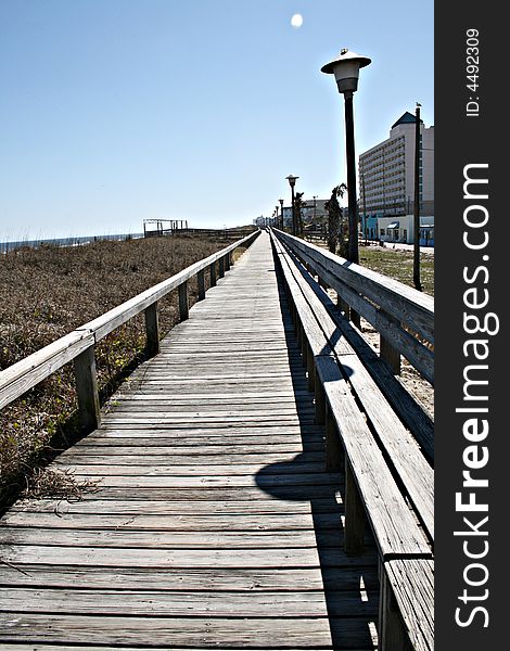 Beach front wood boardwalk along the sandy dunes and buildings. Seat built into walkway.