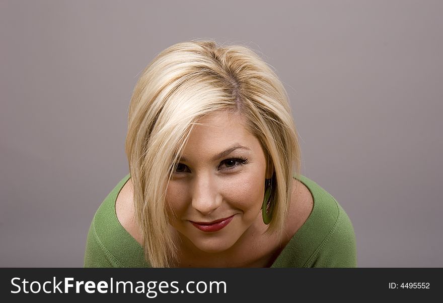 A blonde girl in a green blouse with her head bowed smiling at camera. A blonde girl in a green blouse with her head bowed smiling at camera