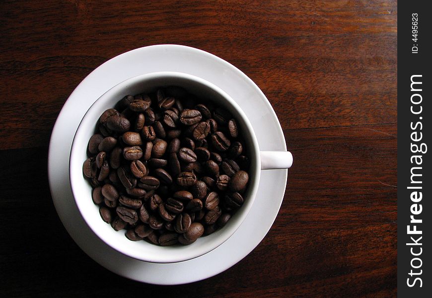 Coffee beans in white cup on wooden surface