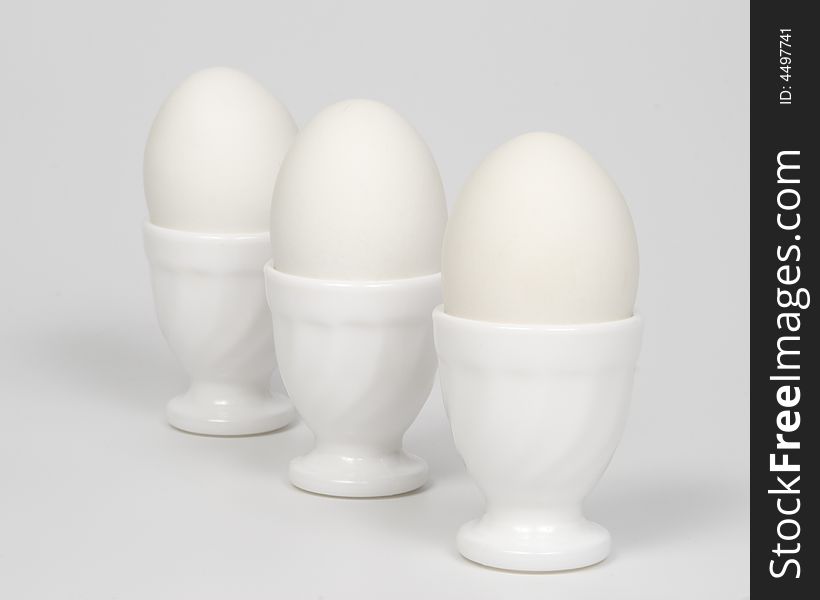 Three white eggs in glass eggcups on a white background. Three white eggs in glass eggcups on a white background.
