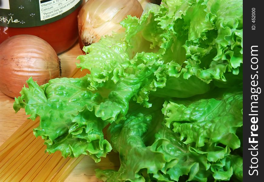 Fresh, crisp head of organic green leaf lettuce and onions along with spaghetti noodles and sauce. Fresh, crisp head of organic green leaf lettuce and onions along with spaghetti noodles and sauce.