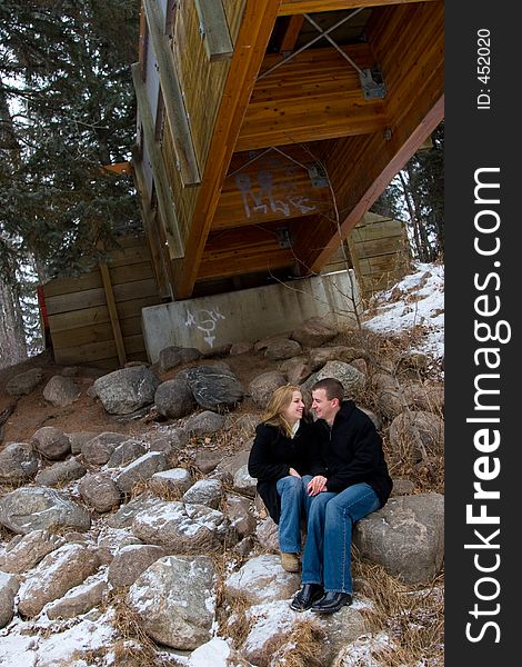 A young couple shares a happy moment together while seated under a bridge in winter. A young couple shares a happy moment together while seated under a bridge in winter.