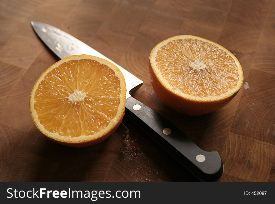 Orange sliced in half with knife on wooden cutting board. Orange sliced in half with knife on wooden cutting board